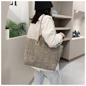 Detailed view of tweed textured tote bag with metal chain strap worn by a model