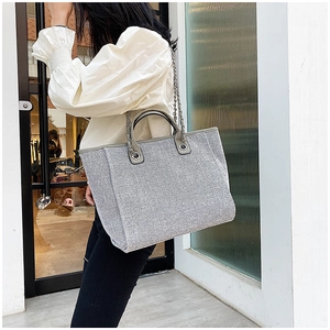 Detail of silver glitter tote bag with leather handle and metal chain on a model