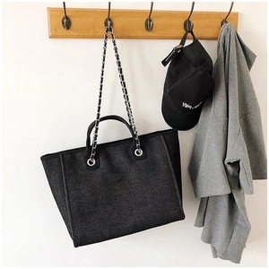 Detail of black trapezoid tote bag with silver chain straps hanging in lifestyle setting