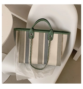Détail du cabas en toile à rayures verticales avec garniture en cuir vert et chaîne en métal