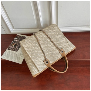Detail of a large woven tote bag featuring beige geometric patterns and brown leather handles
