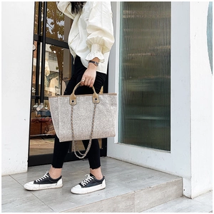 Close-up of oatmeal tote bag with brown leather handles and stylish metal chain detail