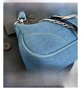 Detailed close-up showing blue denim texture and contrast white stitching on a shoulder bag