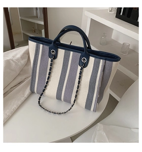Gros plan du sac cabas en toile rayée avec garniture en cuir bleu et chaîne argentée