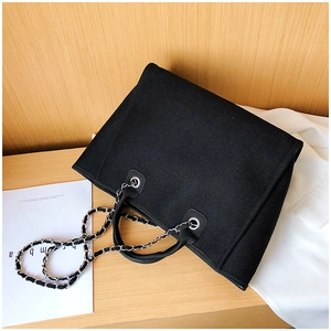 Detail of black woven fabric tote bag with leather handles and metal chain strap