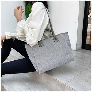 Detail of grey tote bag with shimmering texture, leather handle and metal chain strap