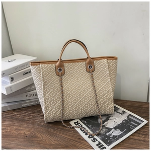 Detail of woven cream tote bag with brown leather trim and silver chain strap