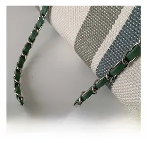 Detail of silver chain strap interwoven with green leather on striped canvas bucket bag