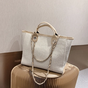 Chic beige tweed tote bag with leather handles and chain strap on a display stand