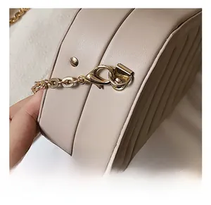 Detailed close-up of golden lobster clasp and flat chain on beige quilted leather bag