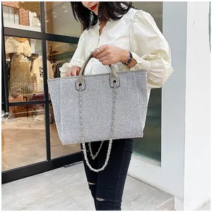 Modern silver glitter tote bag with metallic chain handles shown in a street style view