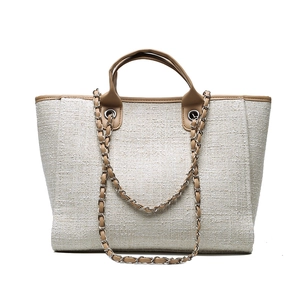 Beige woven tweed tote bag with brown leather handles and decorative metal chains