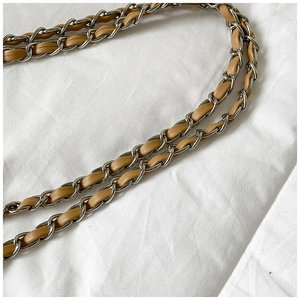 Detail of light brown woven leather strap and silver metal chain links on a bucket bag