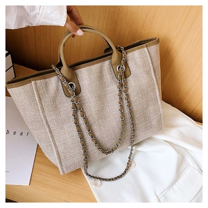 Close-up of beige woven tote bag featuring round handles and silver chain shoulder strap