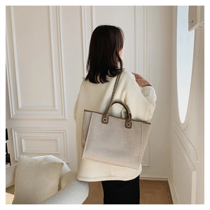Detail of canvas tote bag showing brown leather handles and metal chain decoration