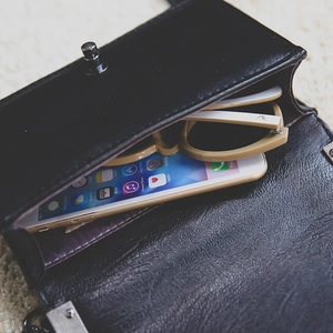 Classic black faux leather crossbody bag with metal lock shown with phone and sunglasses