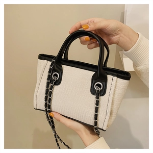 Detail of canvas bucket bag featuring black leather trim and woven metal chain strap