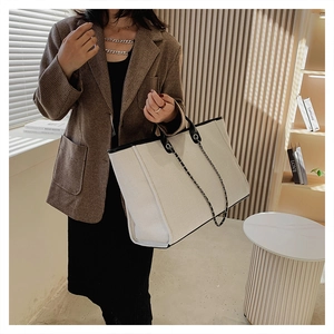 Chic cream canvas tote bag with black leather trim and chain strap shown on a model