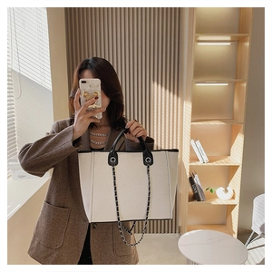 Detailed view of large canvas tote bag with black leather trim and chain shoulder straps