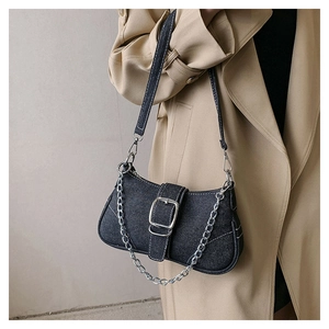 Detail of blue denim shoulder bag with silver buckle and chain on beige coat