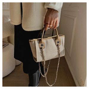 Detail of canvas bucket bag with leather handles and metallic chain shoulder strap