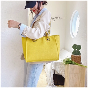Detail of yellow woven tote bag with metal chain strap shown on model shoulder