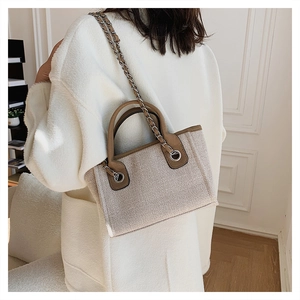 Close-up of beige woven texture tote bag with brown handles and silver chain strap