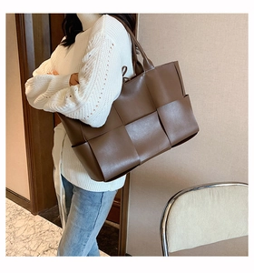 Détail du grand sac cabas tressé marron foncé porté à l'épaule par un mannequin