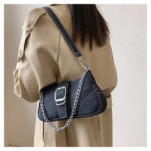 Detail of dark denim shoulder bag with silver buckles and contrast stitching on a beige coat