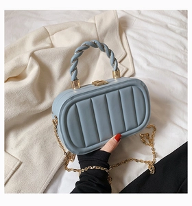 Detail of light blue quilted handbag with twisted handle and golden chain strap