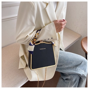 Detail einer schwarzen Trapez-Box-Tasche mit Seidenschal-Griff und goldenem Metallrand