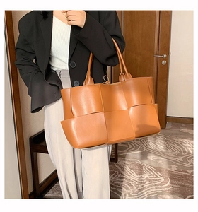 Gros plan sur un grand sac cabas tressé marron caramel avec de larges anses en cuir