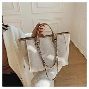 Detail of off-white woven tote bag with brown leather trim and metal chain strap