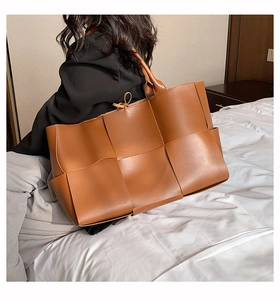 Détail du sac cabas tressé en cuir marron avec larges bandes et nœud de fermeture