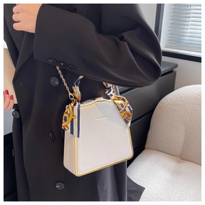 Detail der weißen eckigen Handtasche mit Goldrahmen und dekorativem gebundenem Seidenschal
