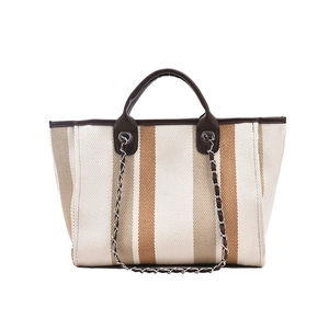 Macro detail of striped canvas tote bag with brown faux leather handles and metal chain