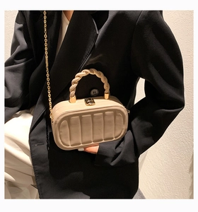 Detail of a beige quilted box bag featuring a braided handle and gold chain strap