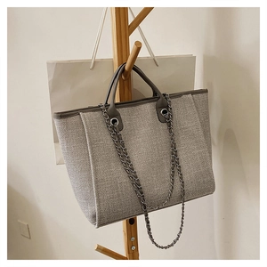 Detail view of grey tweed bucket bag with leather handles and chain strap on a wooden rack