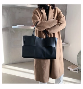 Détail d'un grand sac cabas noir en cuir tressé porté à l'épaule par un mannequin