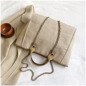 Detail of beige woven tote bag with chain strap and leather handles on soft cloth