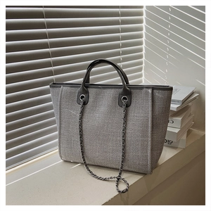 Detailed view of grey woven tweed tote bag with metal chain strap and top handles