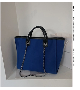 Detail of blue canvas tote bag showing black leather handles and metal chain strap