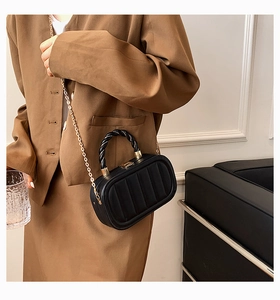 Elegant black box shoulder bag with quilted texture and gold chain on a female model