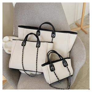 Three sizes of beige canvas bucket bags with black leather trim on a grey sofa