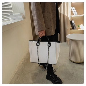 Close-up of large canvas tote bag with black trim and elegant leather chain handle