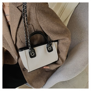 Close-up of minimalist canvas tote bag with black leather trim and metal chain detail