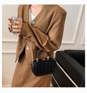 Detail of black vertical quilted chain bag featuring a twisted handle and gold clasp