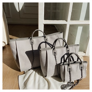 Three sizes of canvas tote bags with leather trim and chain straps in a bright room