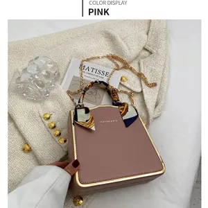Elegante rosa Trapez-Handtasche mit Goldrand und Seidenschal-Griff auf weißem Stoff