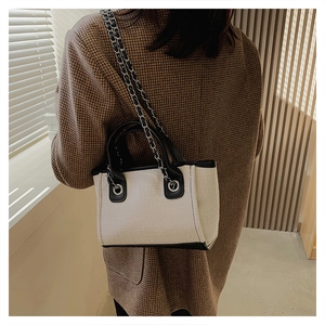 Detail of canvas tote bag with black leather trim and silver chain strap on model